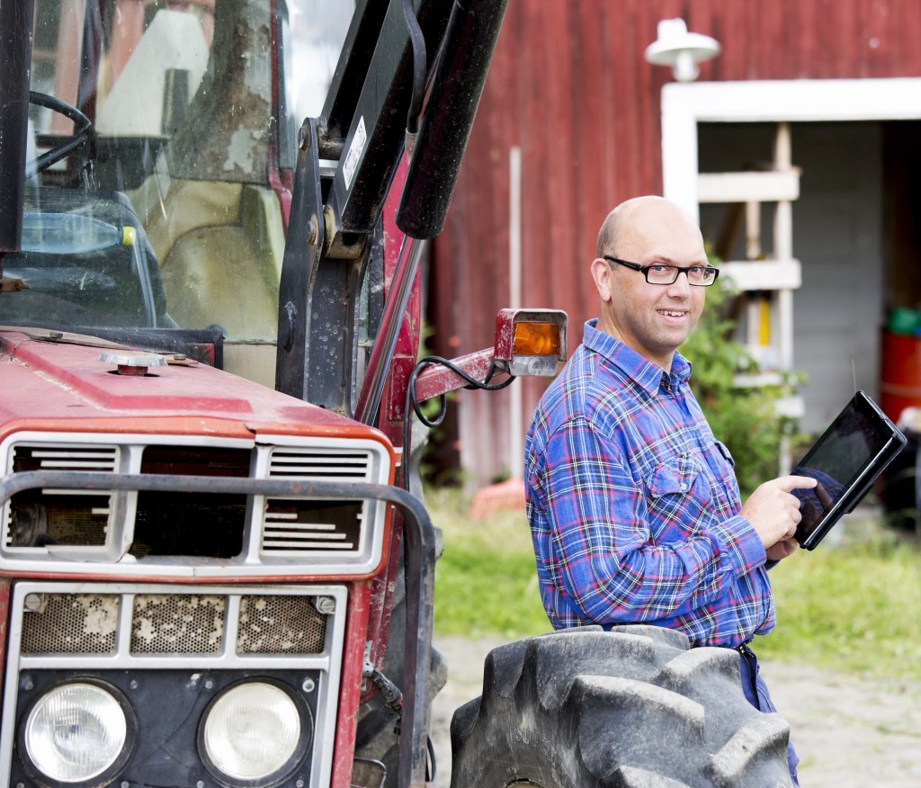 Lantbrukare vid traktor, skriver på en Ipad